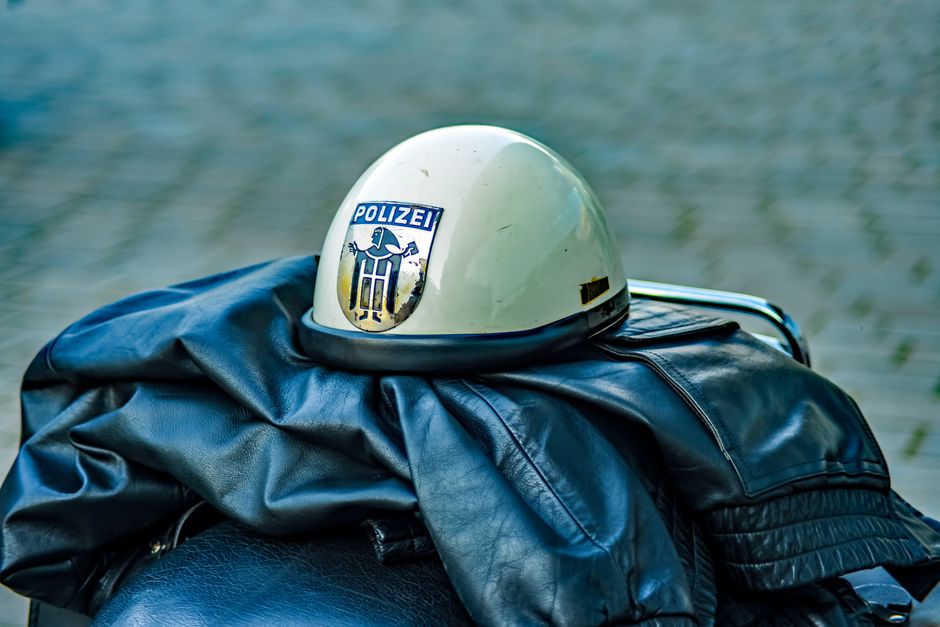 Retro police helmet with insignia resting on a leather jacket outdoors.