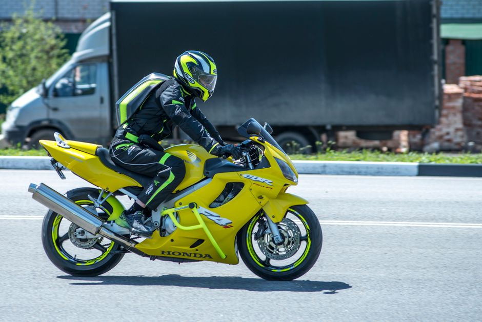 A rider in a racing suit and helmet drives a yellow sports bike outdoors.