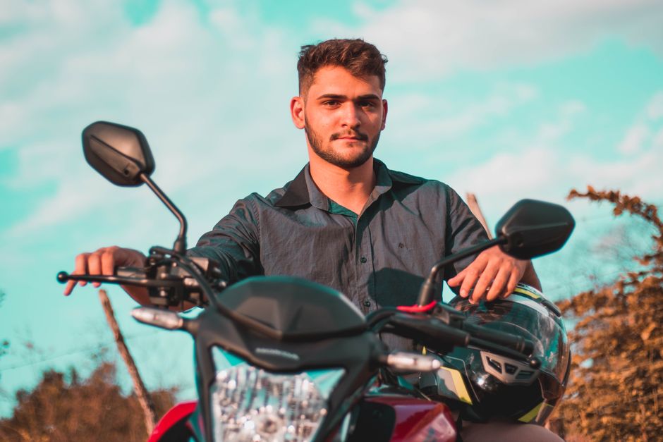 Young male motorcyclist sits confidently on his bike with a helmet outdoors under a clear sky.