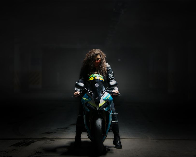 A woman confidently rides a sleek motorcycle under dramatic lighting.