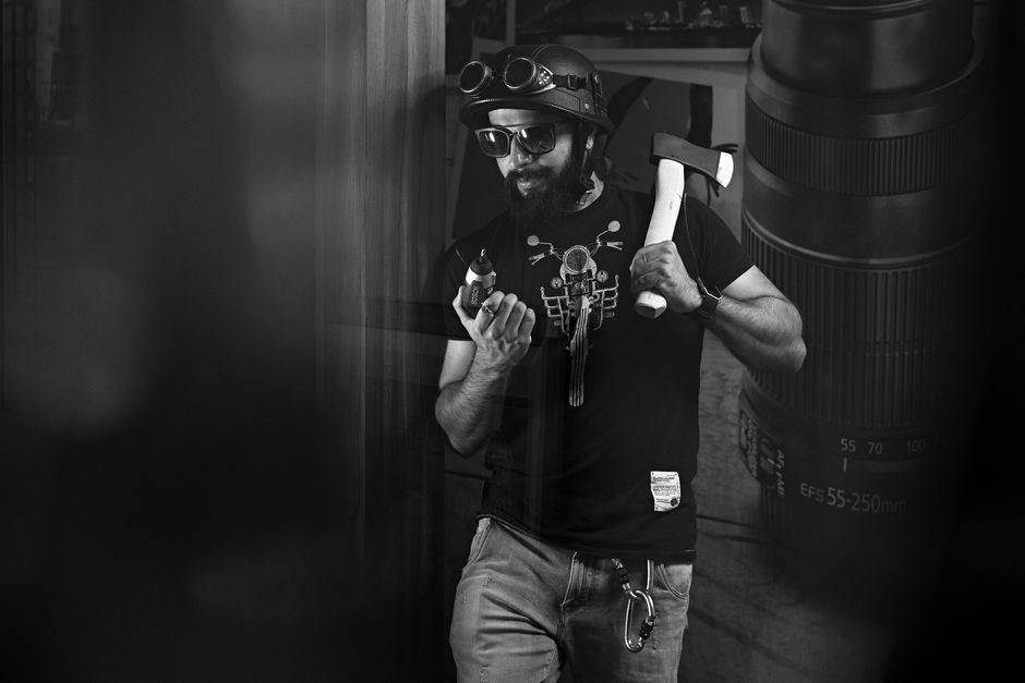 Black and white image of a man with tools and camera gear, exuding a rugged and creative vibe.